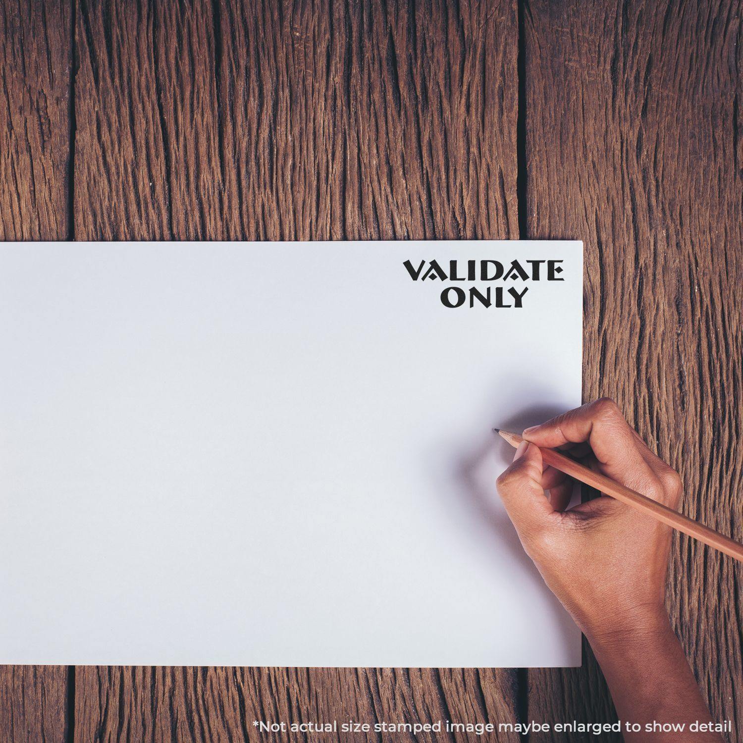 Hand holding a pencil next to a VALIDATE ONLY rubber stamp mark on a white paper, placed on a wooden surface.