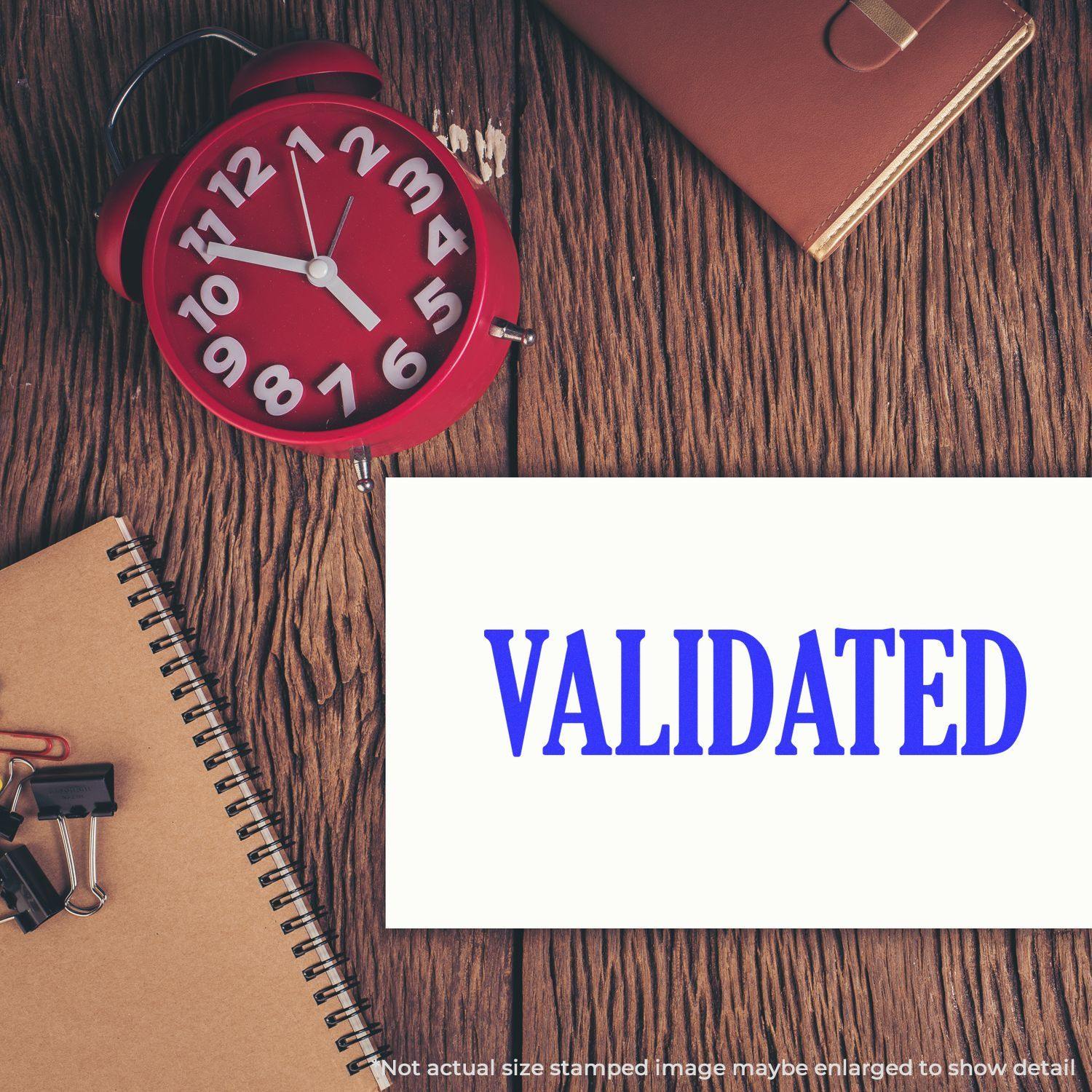 Slim Pre-Inked Validated Stamp used on a white paper beside a red clock, notebook, and office supplies on a wooden desk.