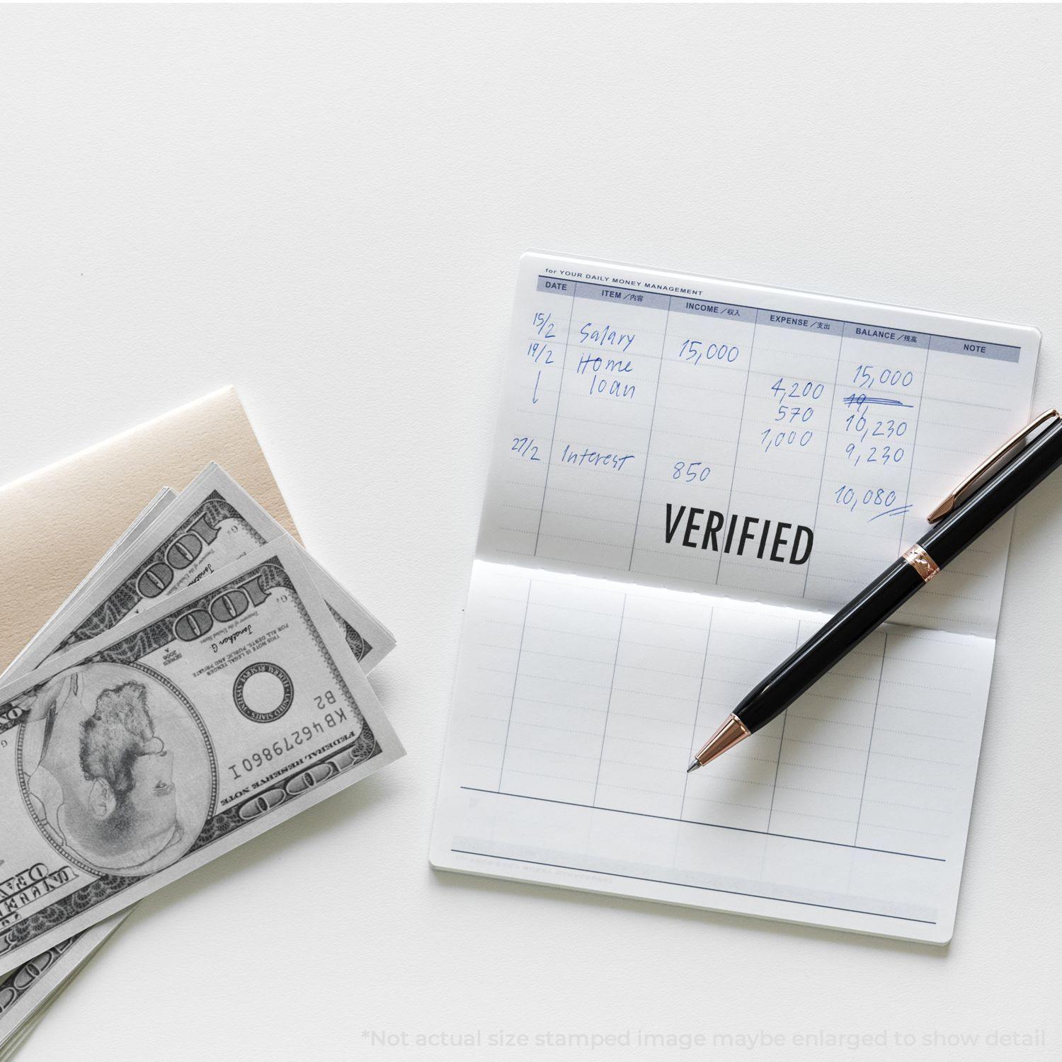 Verified rubber stamp on a financial ledger with handwritten entries, a pen, and a stack of hundred-dollar bills nearby.