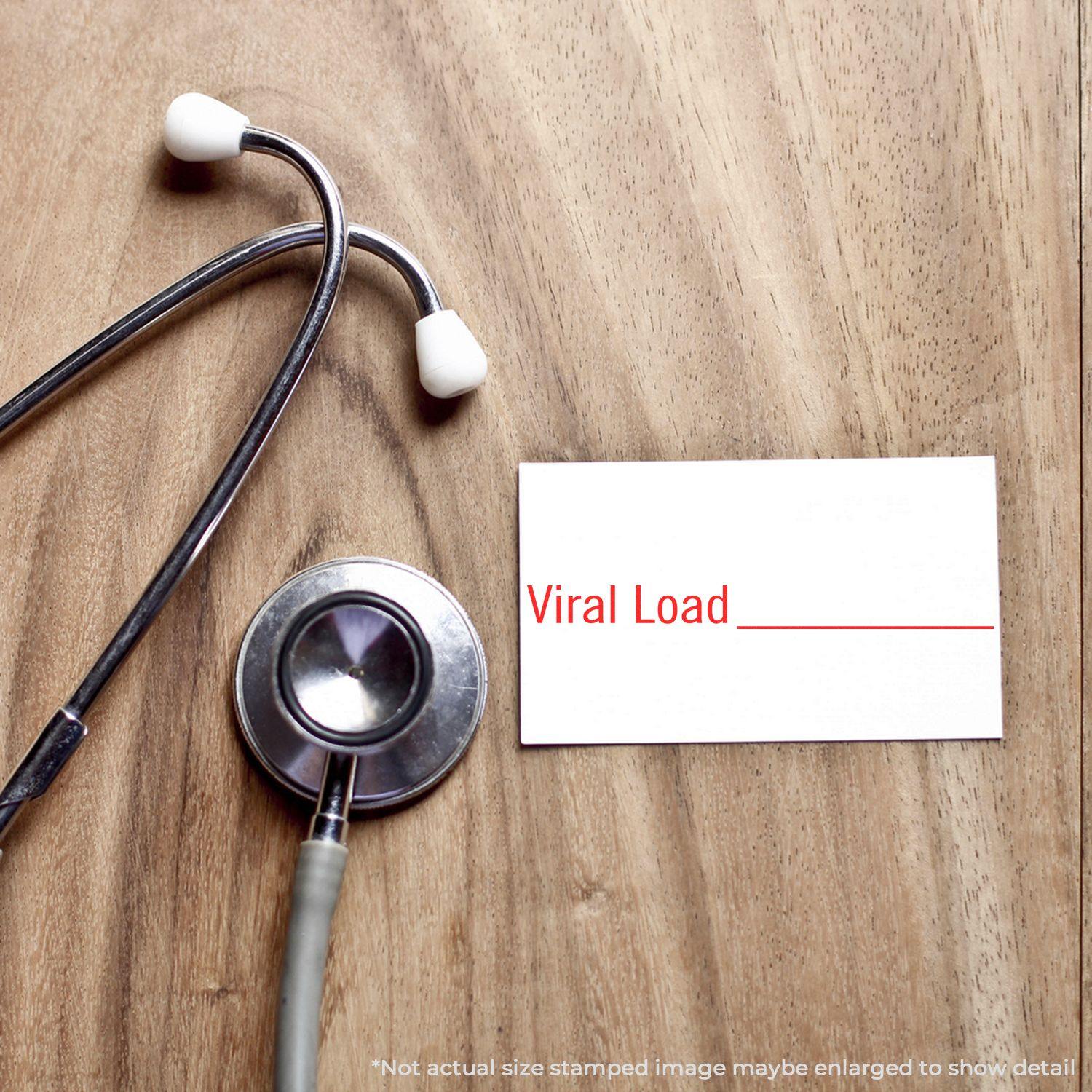 A Large Pre-Inked Viral Load Stamp next to a stethoscope on a wooden surface, with Viral Load stamped in red on a white card.