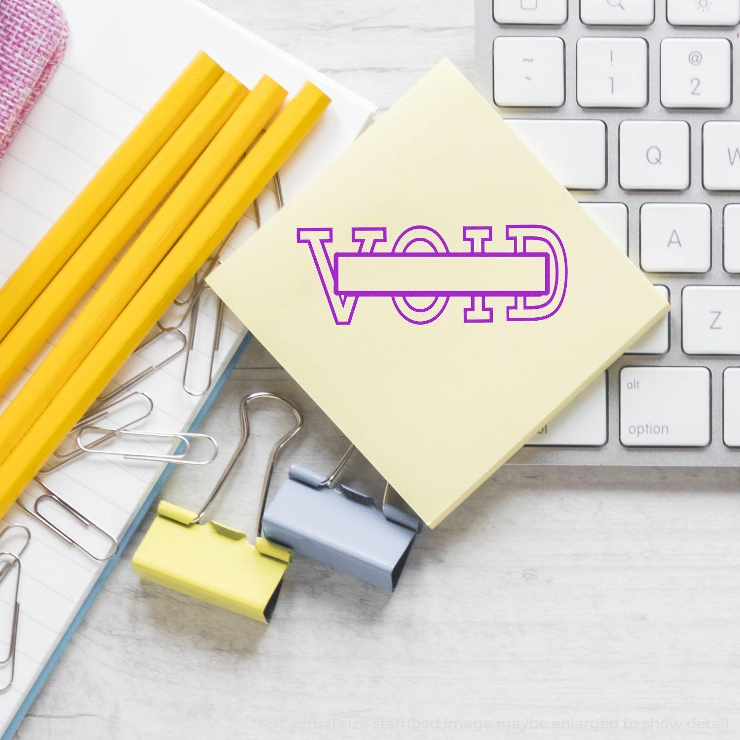 Self Inking Void with Box Stamp on a yellow sticky note, surrounded by pencils, paper clips, binder clips, and a keyboard.