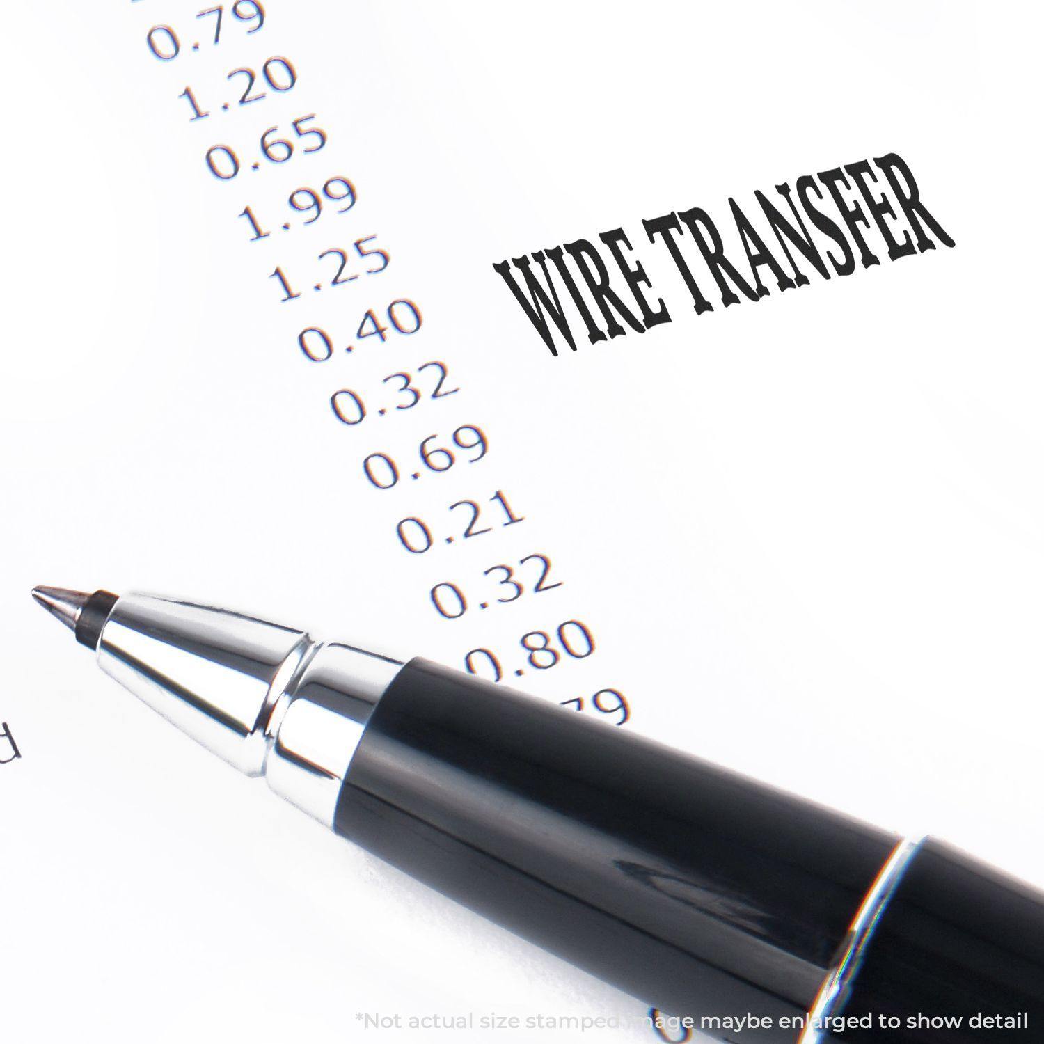 Pen next to a Slim Pre-Inked Wire Transfer Stamp on a document with numbers, showing the stamped text WIRE TRANSFER.