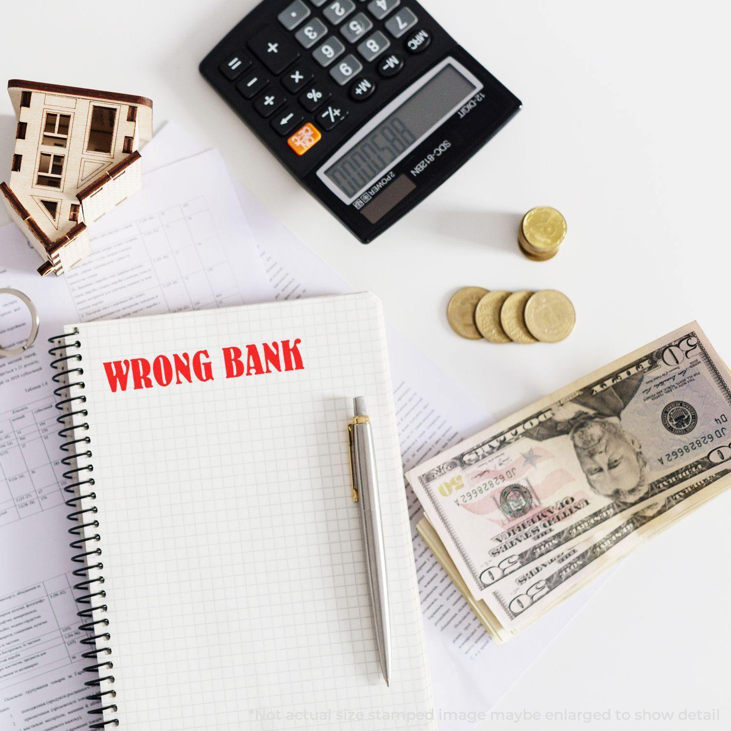 Notebook with WRONG BANK stamped in red using a Slim Pre-Inked Wrong Bank Stamp, surrounded by money, calculator, and documents.