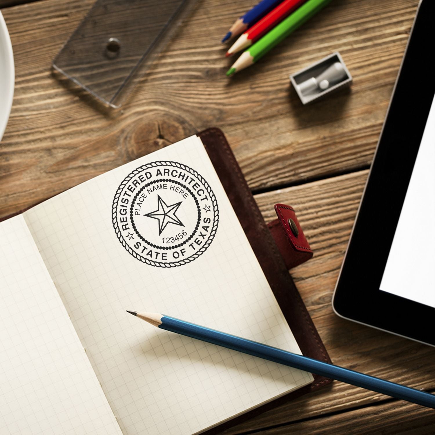 Premium MaxLight Pre-Inked Texas Architectural Stamp in use on a notebook, surrounded by pencils, a sharpener, and a tablet on a wooden desk.