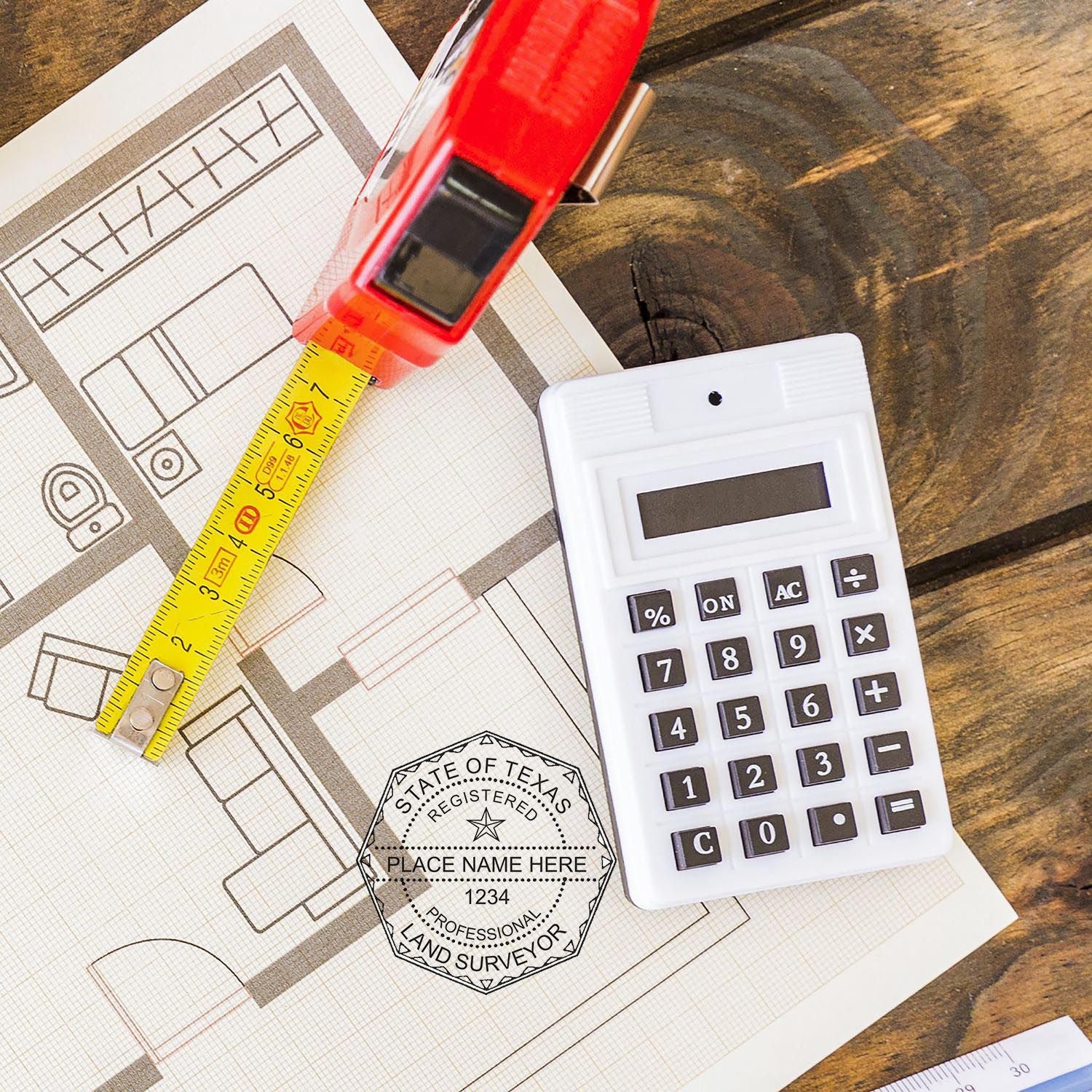 Self Inking Texas Land Surveyor Stamp on a blueprint with a tape measure, calculator, and ruler on a wooden table.