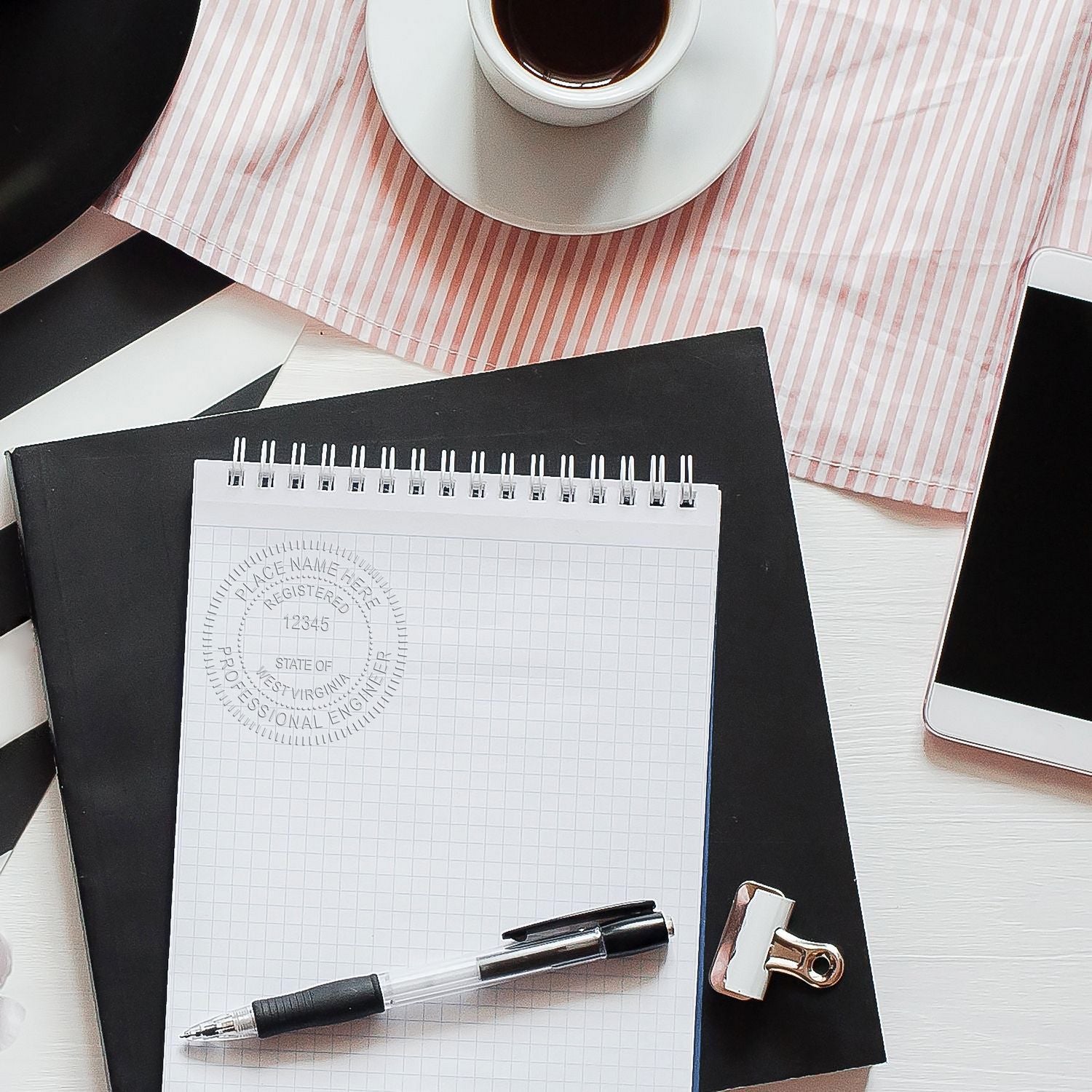 A Professional Engineer Red Soft Seal Embosser imprint is visible on a notepad placed on a desk with a pen, clipboard, smartphone, and a cup of coffee.