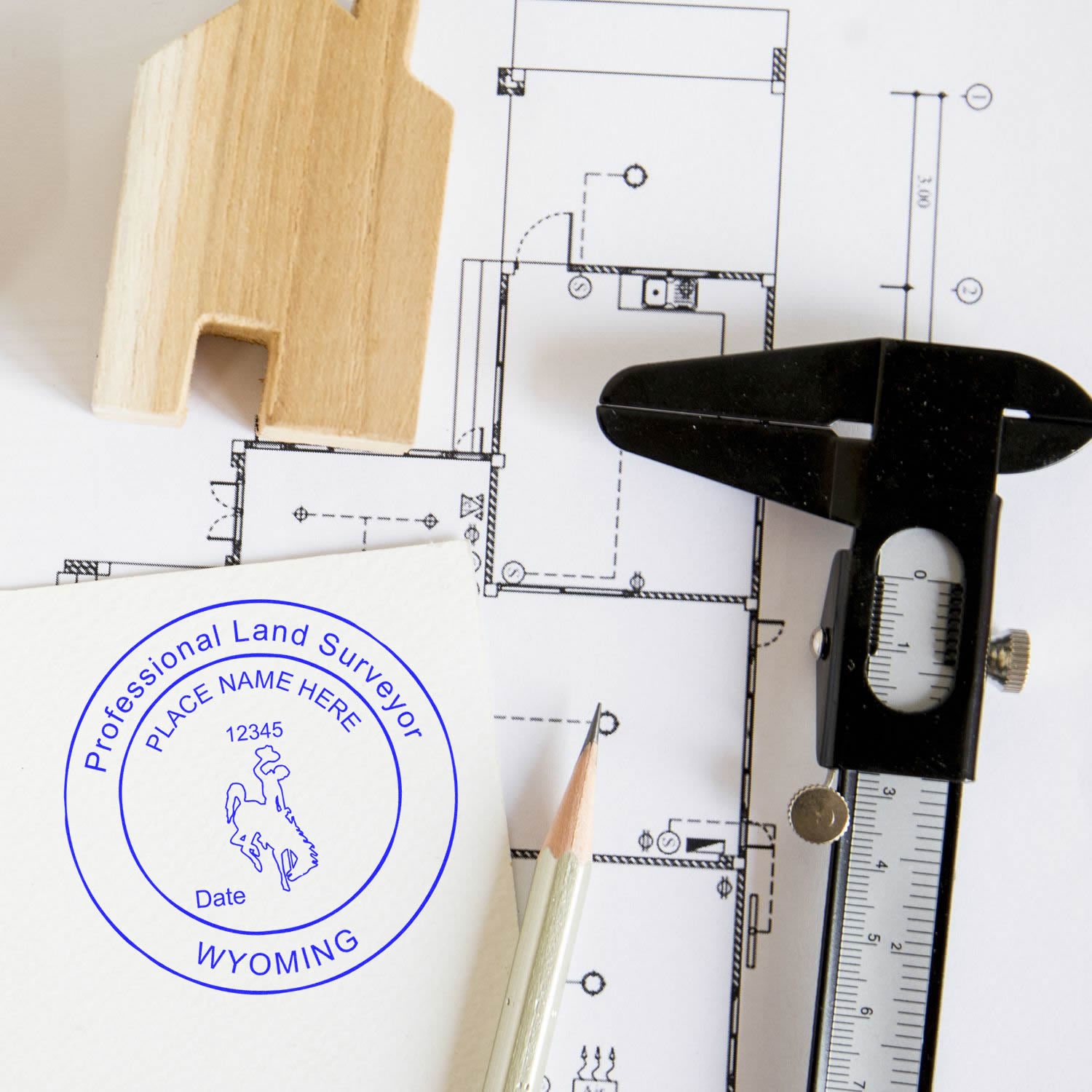 Wyoming Land Surveyor Seal Stamp, WY PLS Stamp on paper with architectural plans, a pencil, a caliper, and a wooden house model.