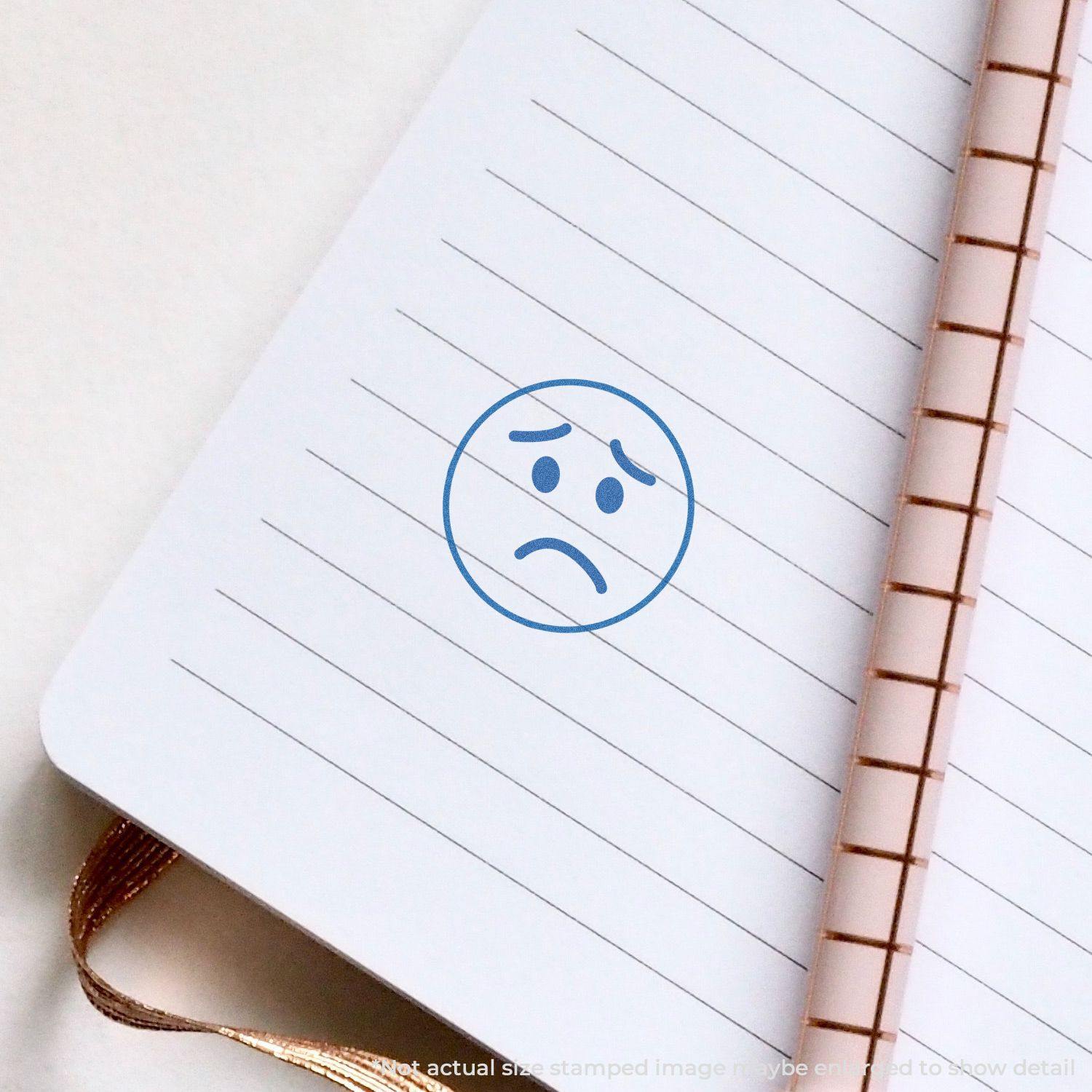 Round Frown Face Xstamper Stamp impression on a lined notebook page, showing a blue frowning face.