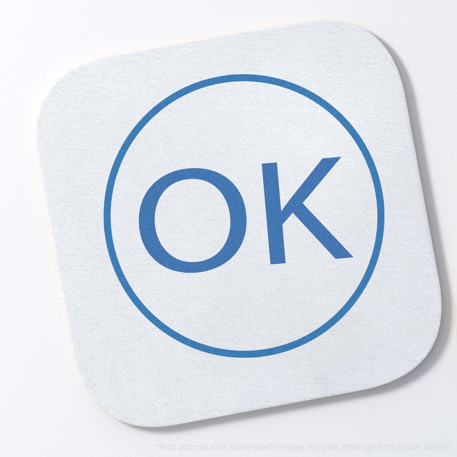 Round Ok Xstamper Stamp imprint on a white square paper, showing a blue OK inside a circle.