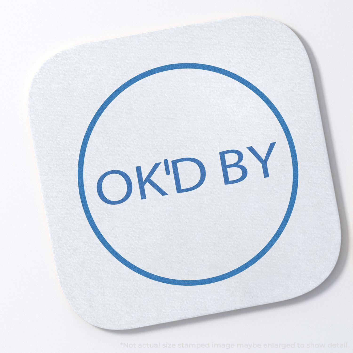 Round OK'D By Xstamper Stamp imprint on a white square paper, showing a blue circular border with the text OK'D BY inside.